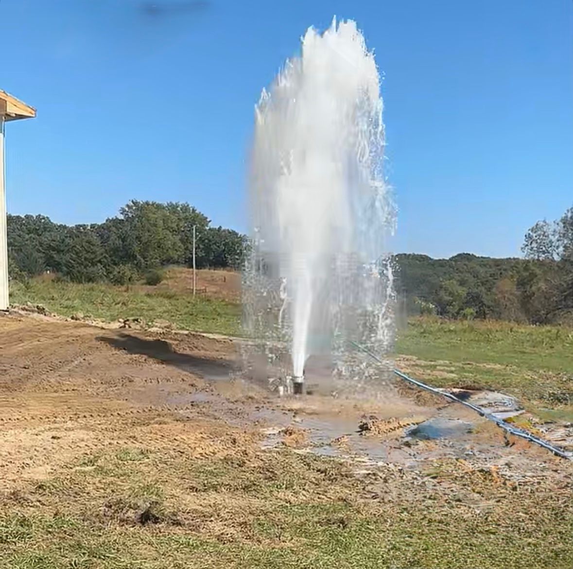 A geyser of water erupts from the ground in a field on a sunny day.