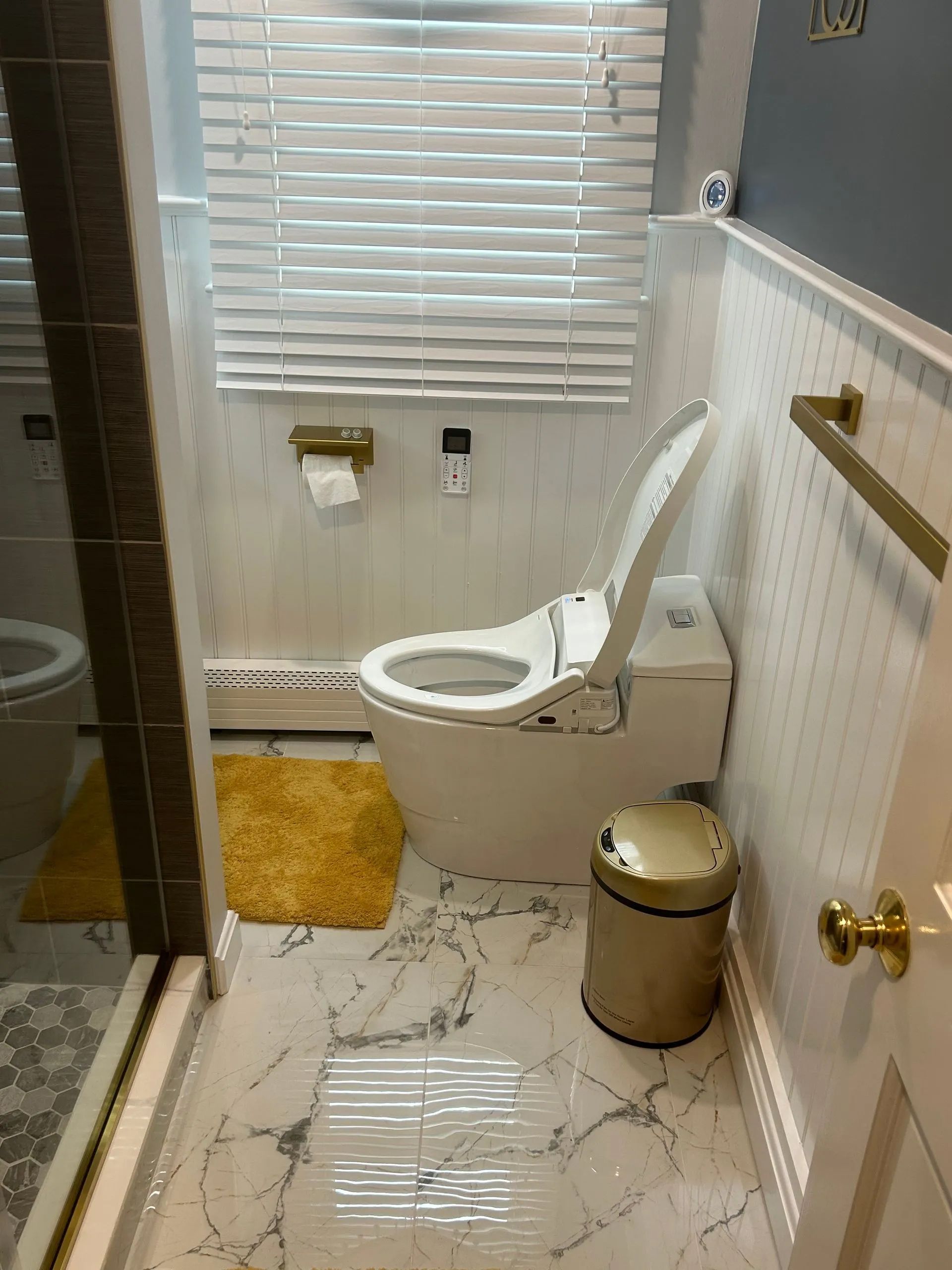 Bathroom with a white toilet, gold accents, marble floor, and yellow rug.