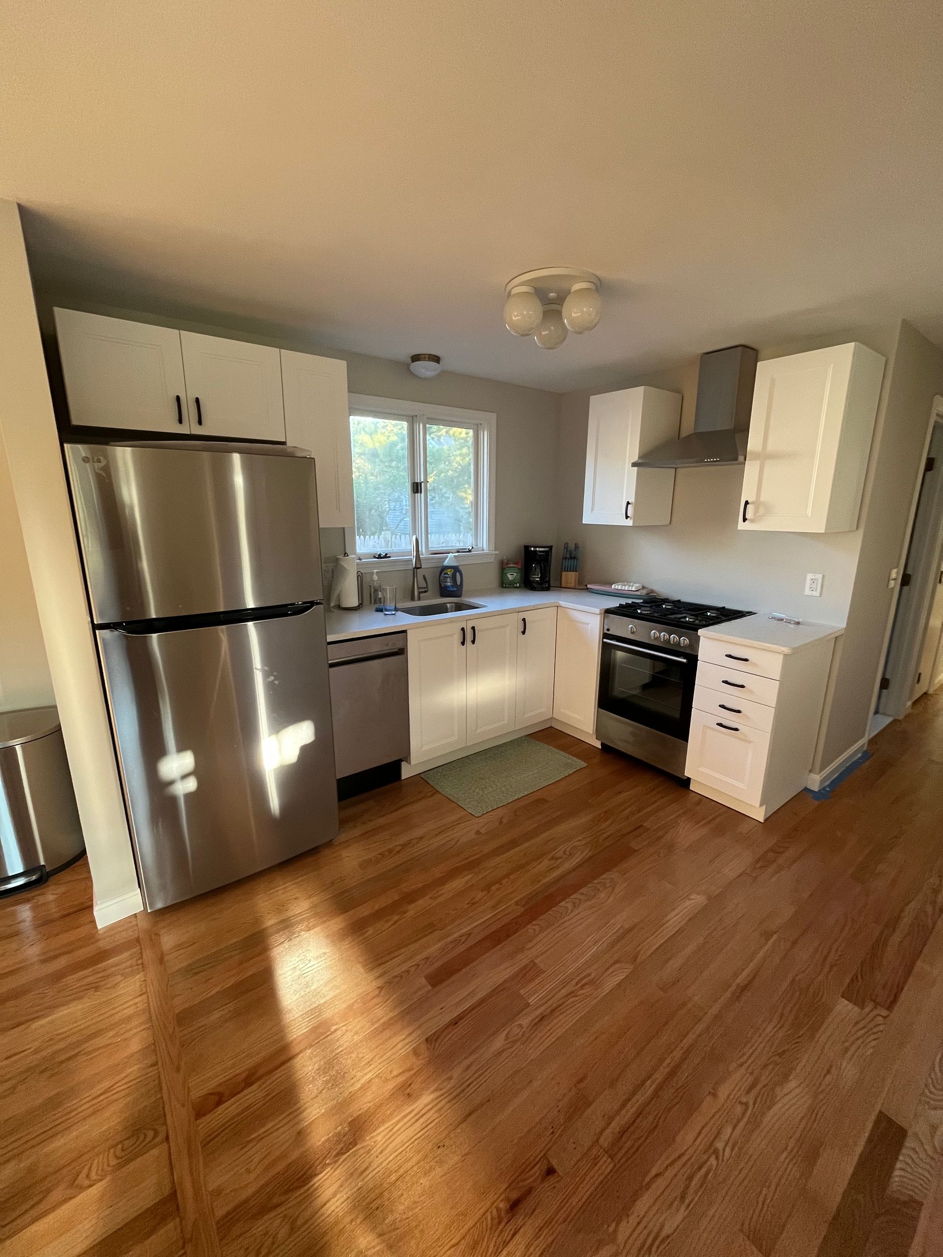 A kitchen with white cabinets, stainless steel appliances, and wood flooring.