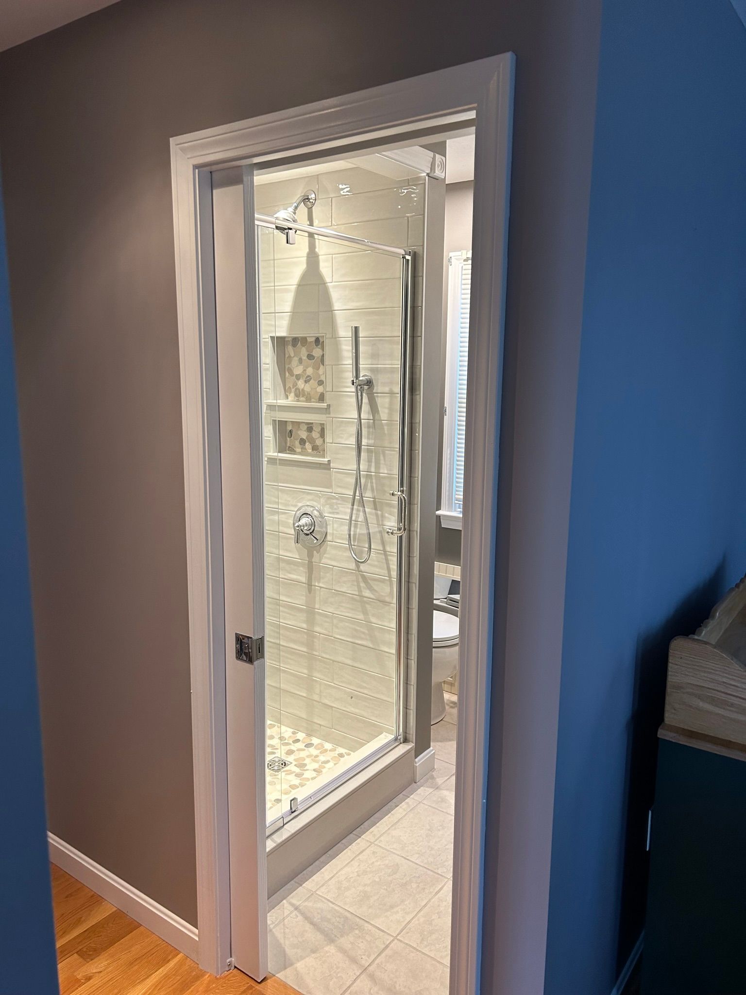Bathroom door with glass shower enclosure and white tile. Grey and blue walls.