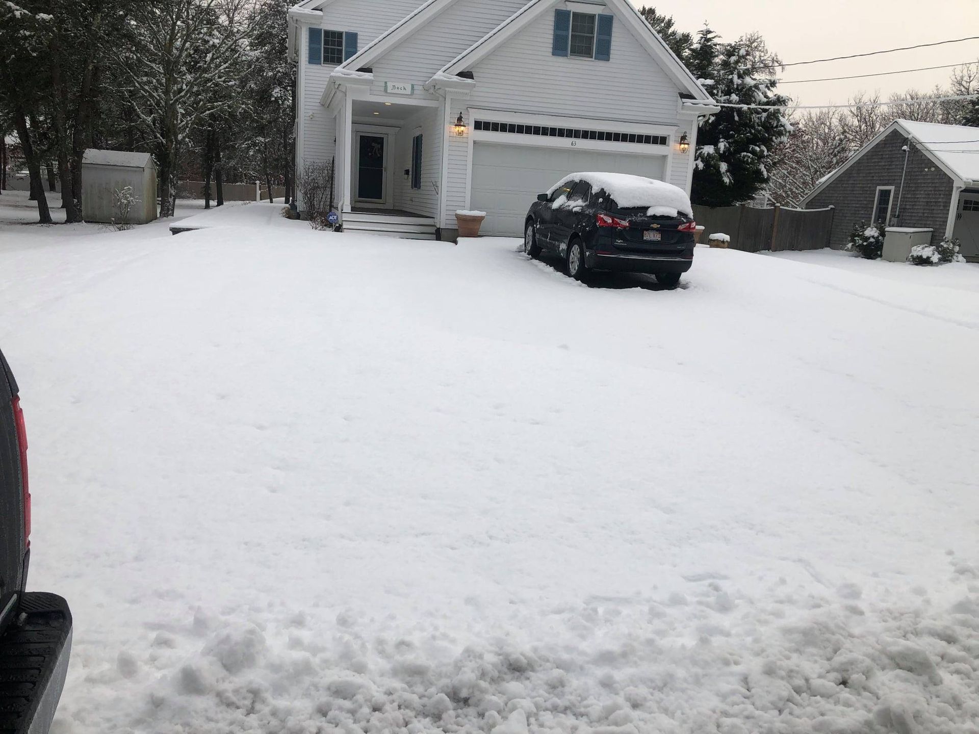 Snow-covered driveway in front of a white house with a car parked in it.