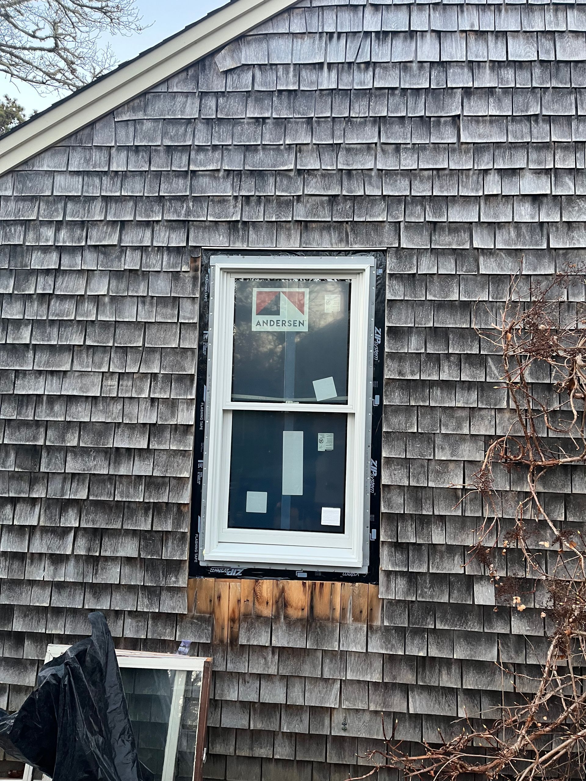 Window installation on a gray shingled house; black sealant around the white frame.