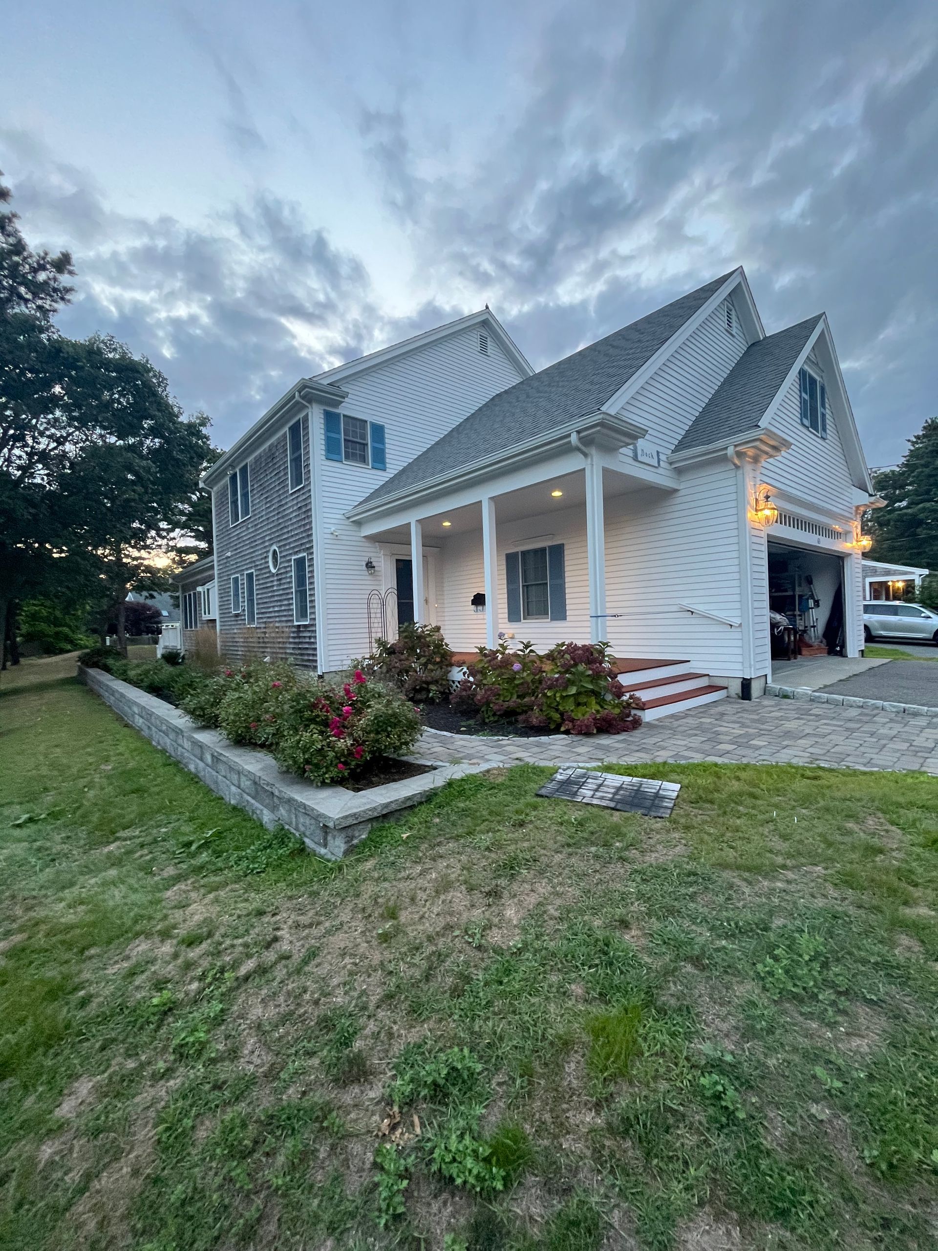 Two-story white house with a porch and attached garage on a cloudy day. Landscaping in front.
