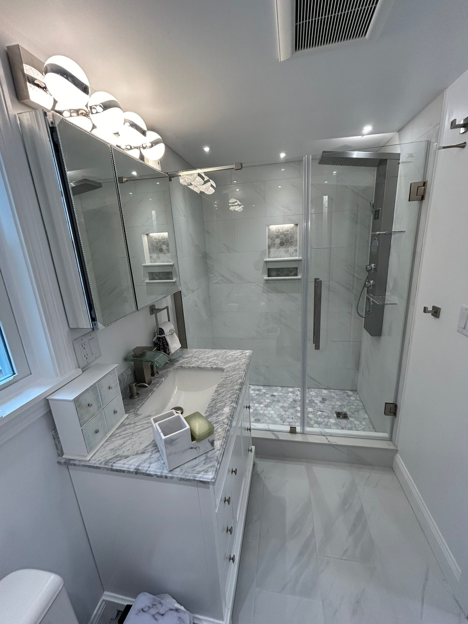 Modern bathroom with a white vanity, marble tile shower, and glass door.