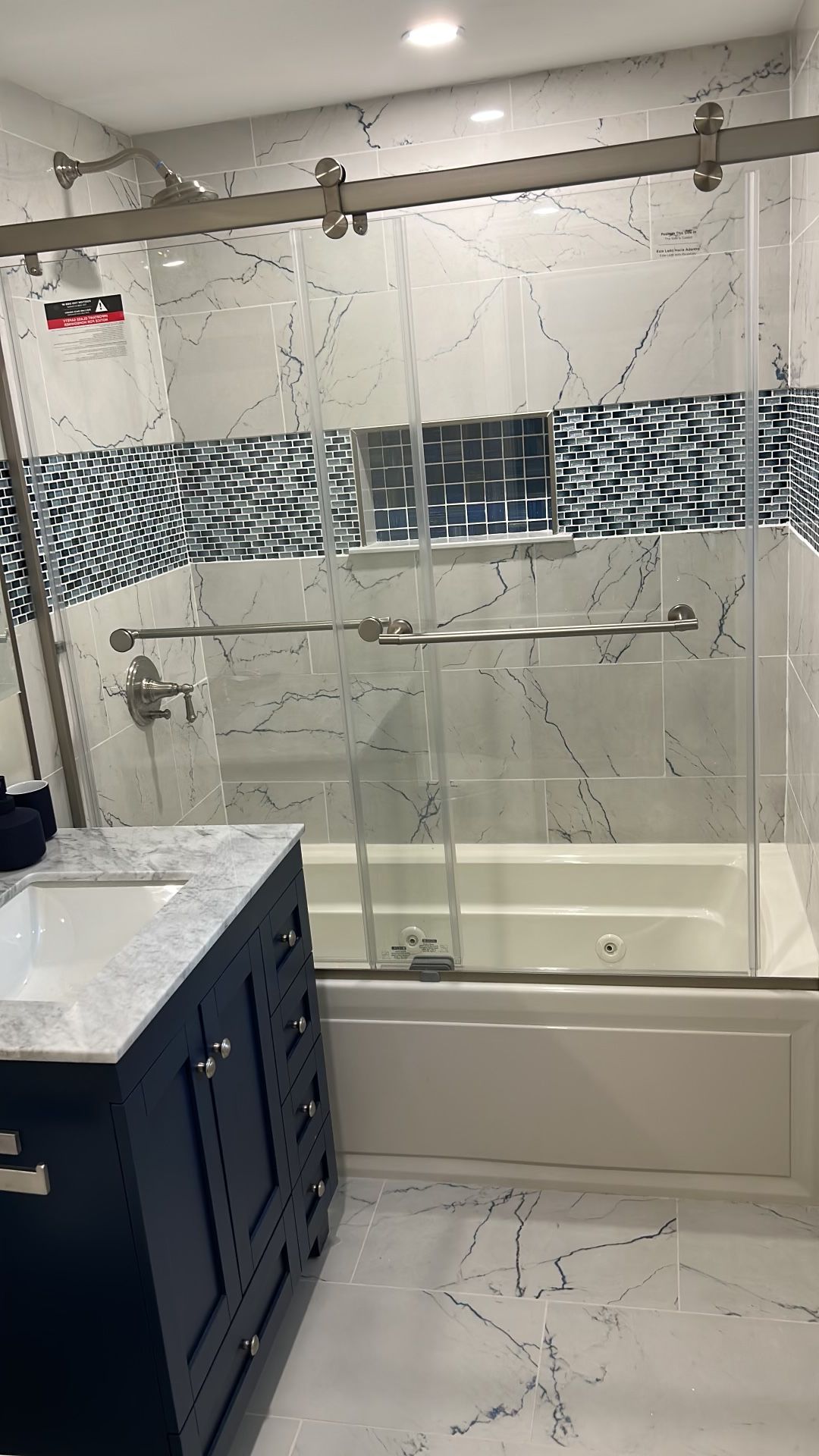 Bathroom with marble-look tile, blue vanity, glass shower doors, and accent tile.
