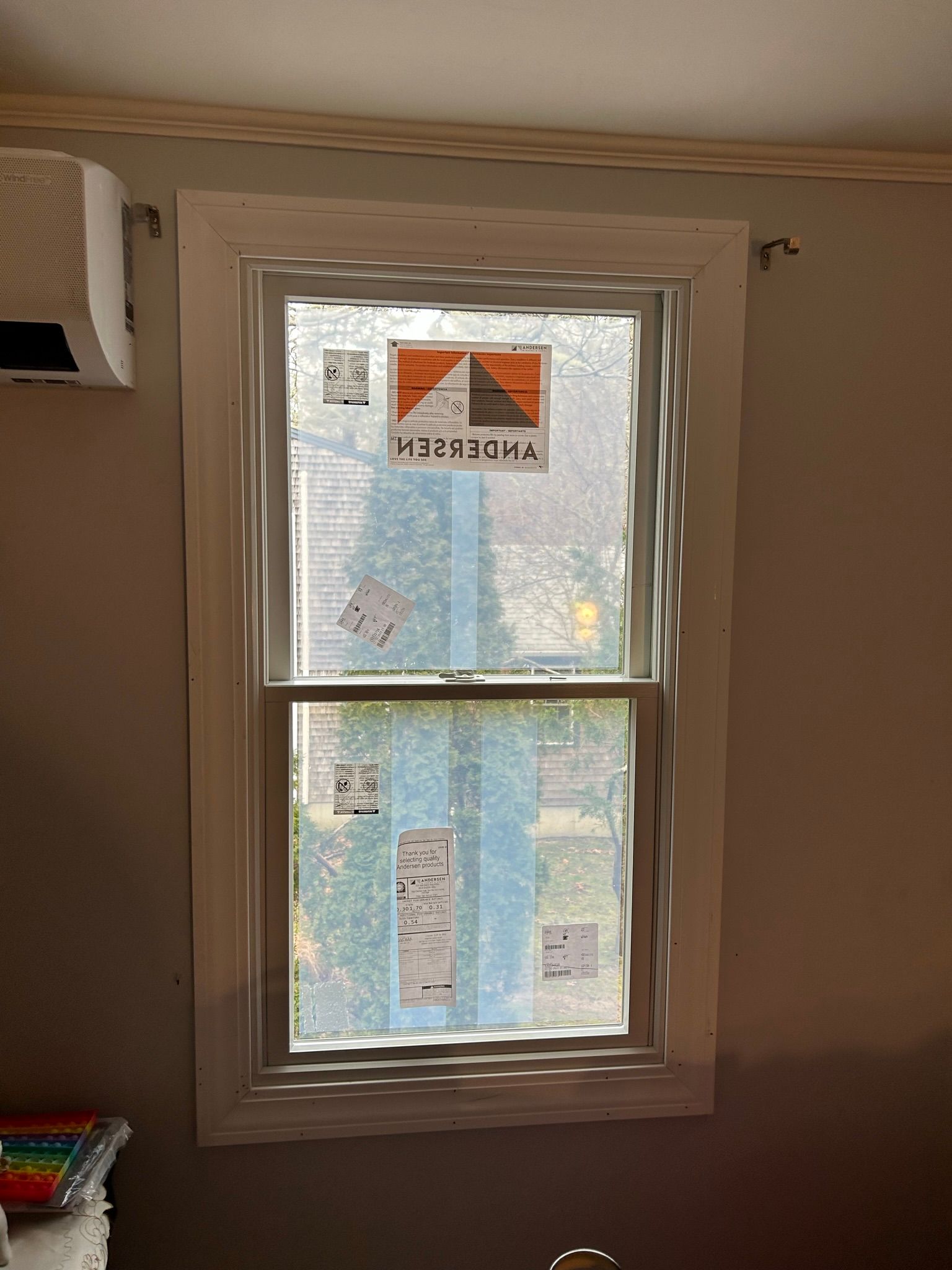 Newly installed window with white trim, covered in protective film, in a room with gray walls.
