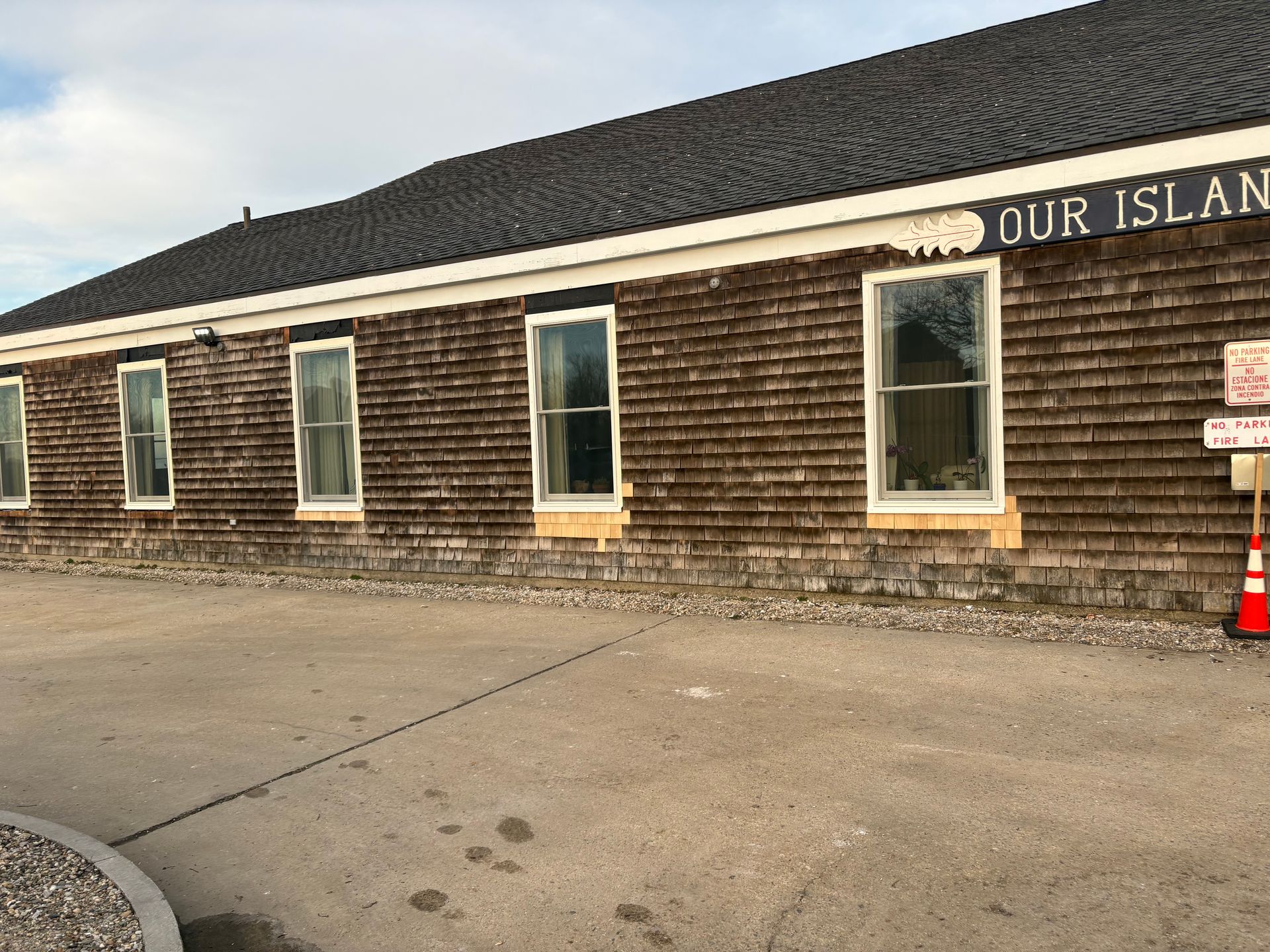 A brown, shingled building with a dark roof and large windows, partially displaying the text 