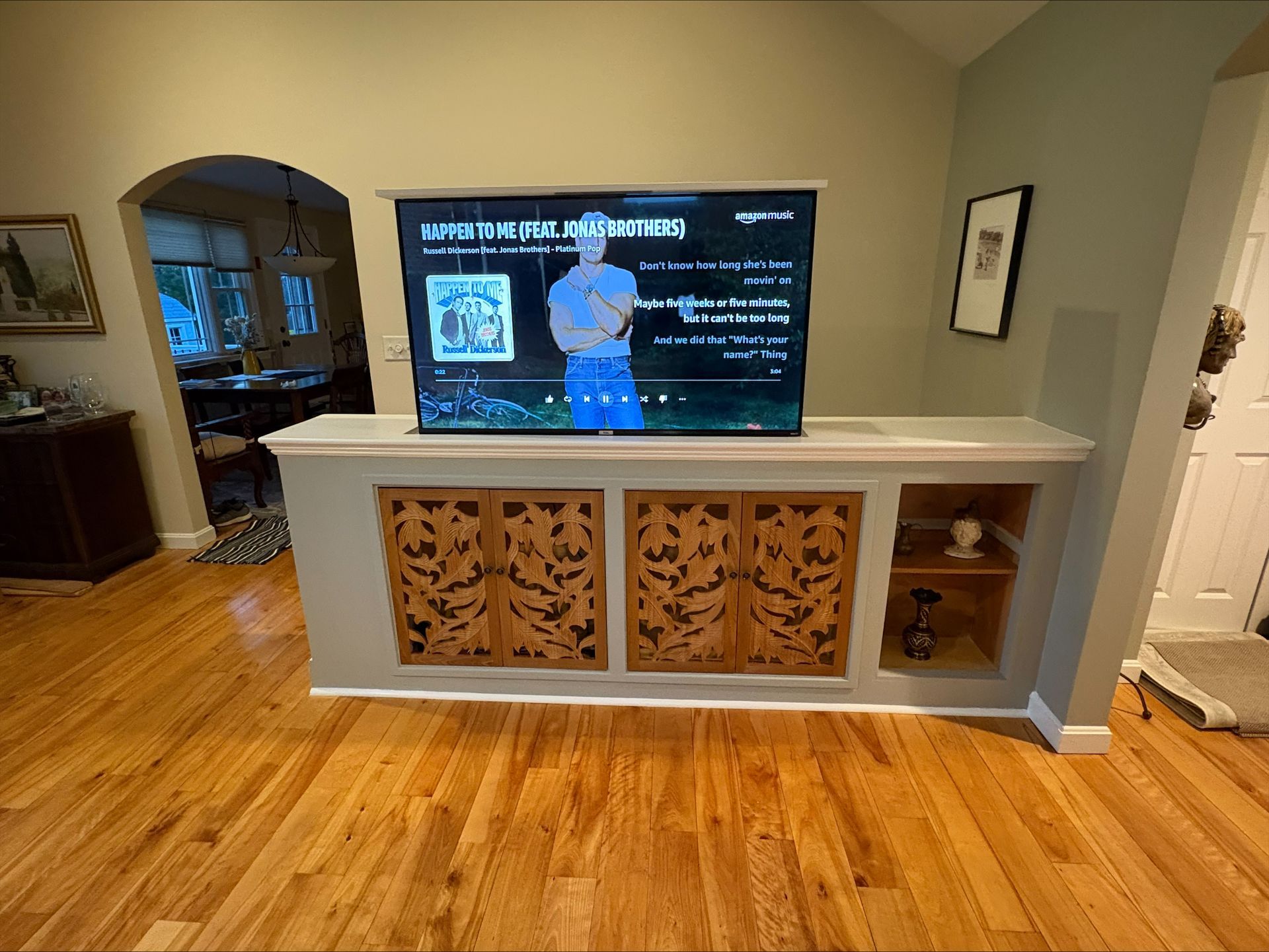 Living room with hardwood floors, a TV on a white console, and decorative carved cabinet panels.