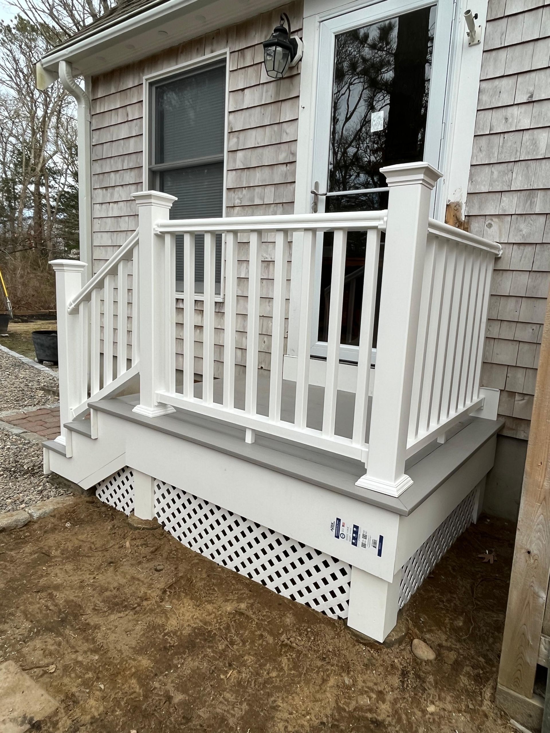 A newly constructed white porch with railings and lattice skirting attached to a house with shingle siding.