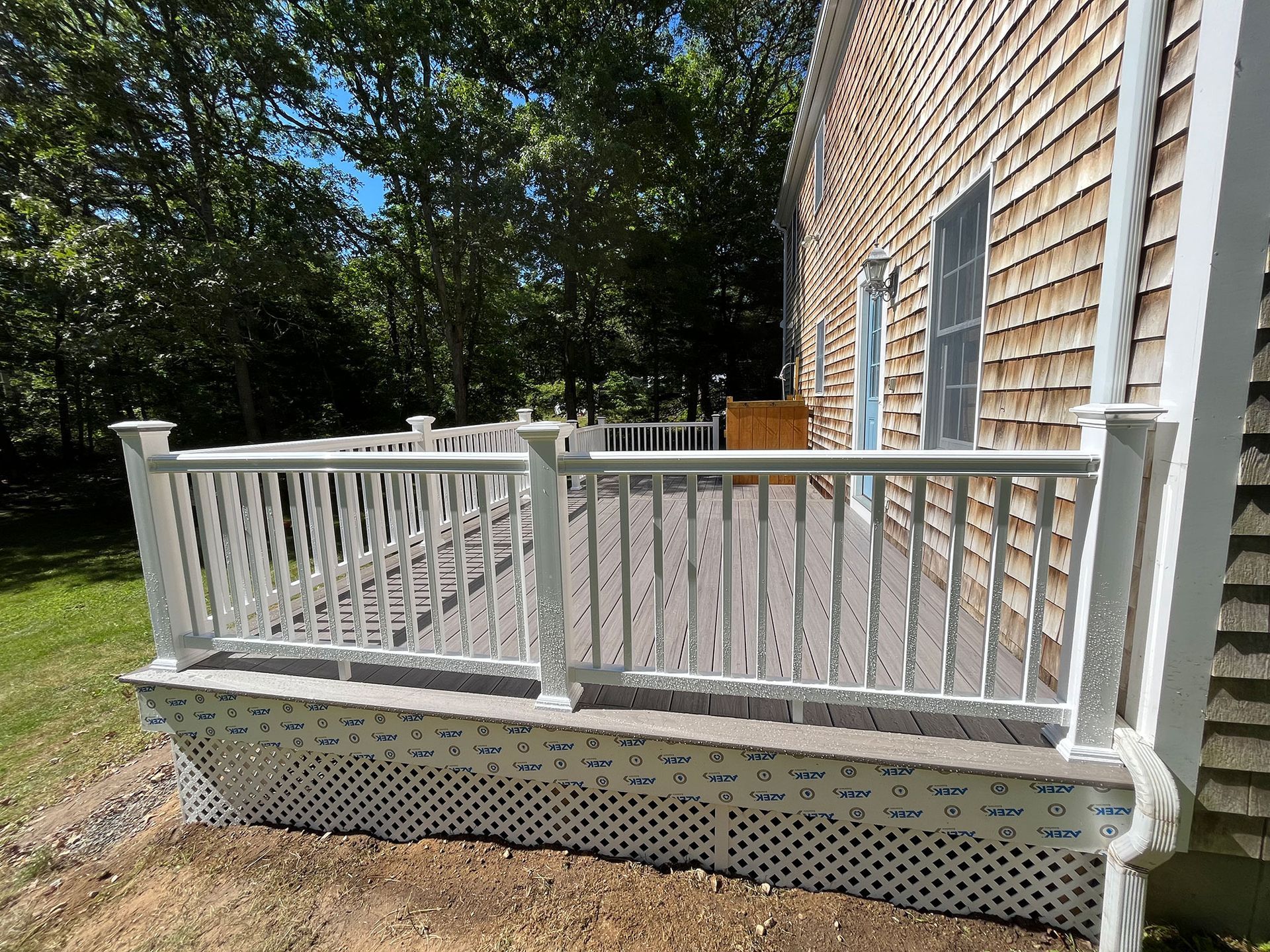 White deck with railings attached to a shingled house.
