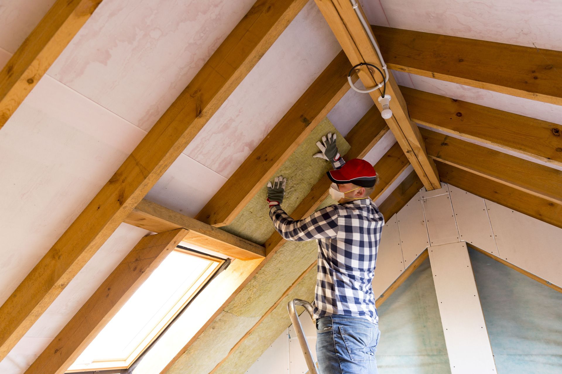 Person installing insulation in a roof with a ladder; indoors.