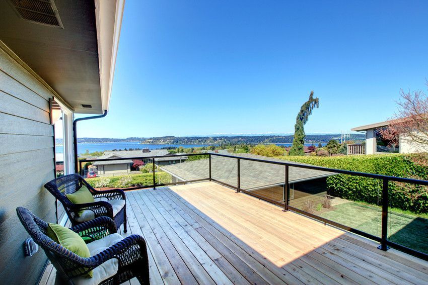 A wooden deck with chairs and a glass railing overlooking a body of water.