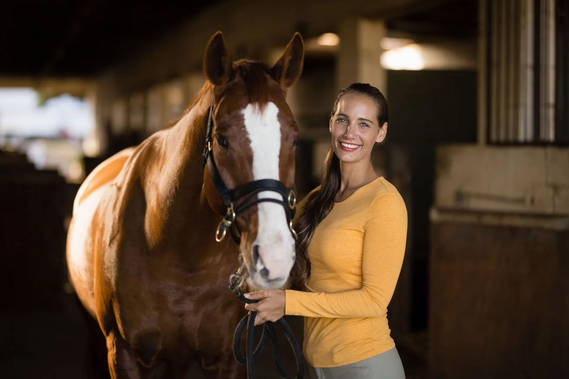 A woman is standing next to a brown horse in a stable