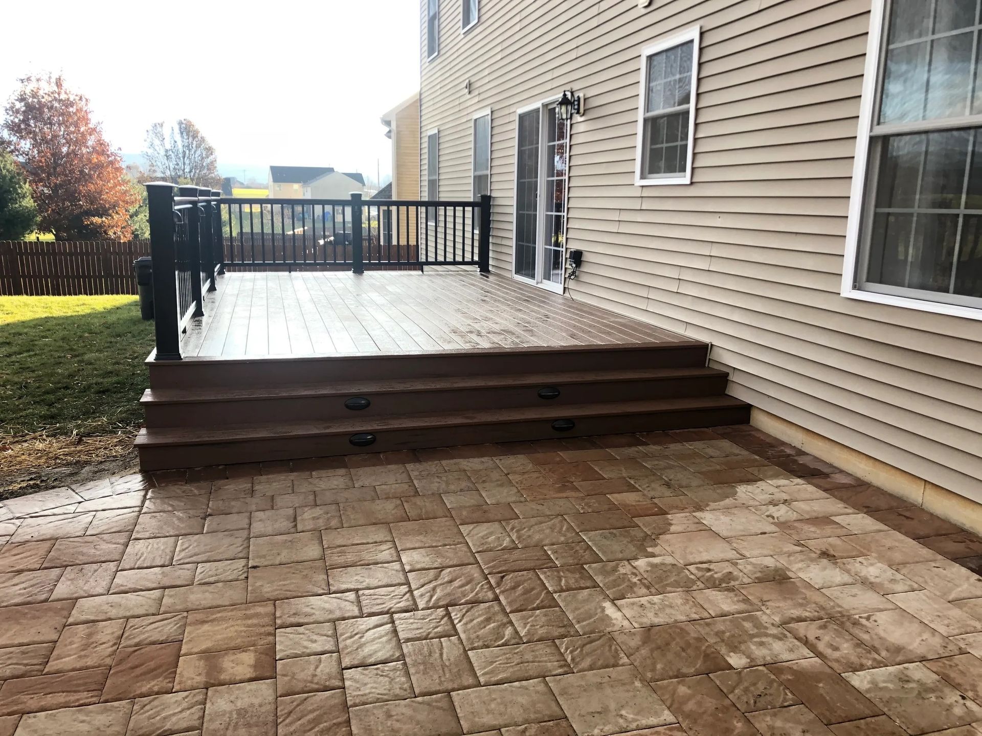 A large deck with stairs leading up to it is in the backyard of a house.