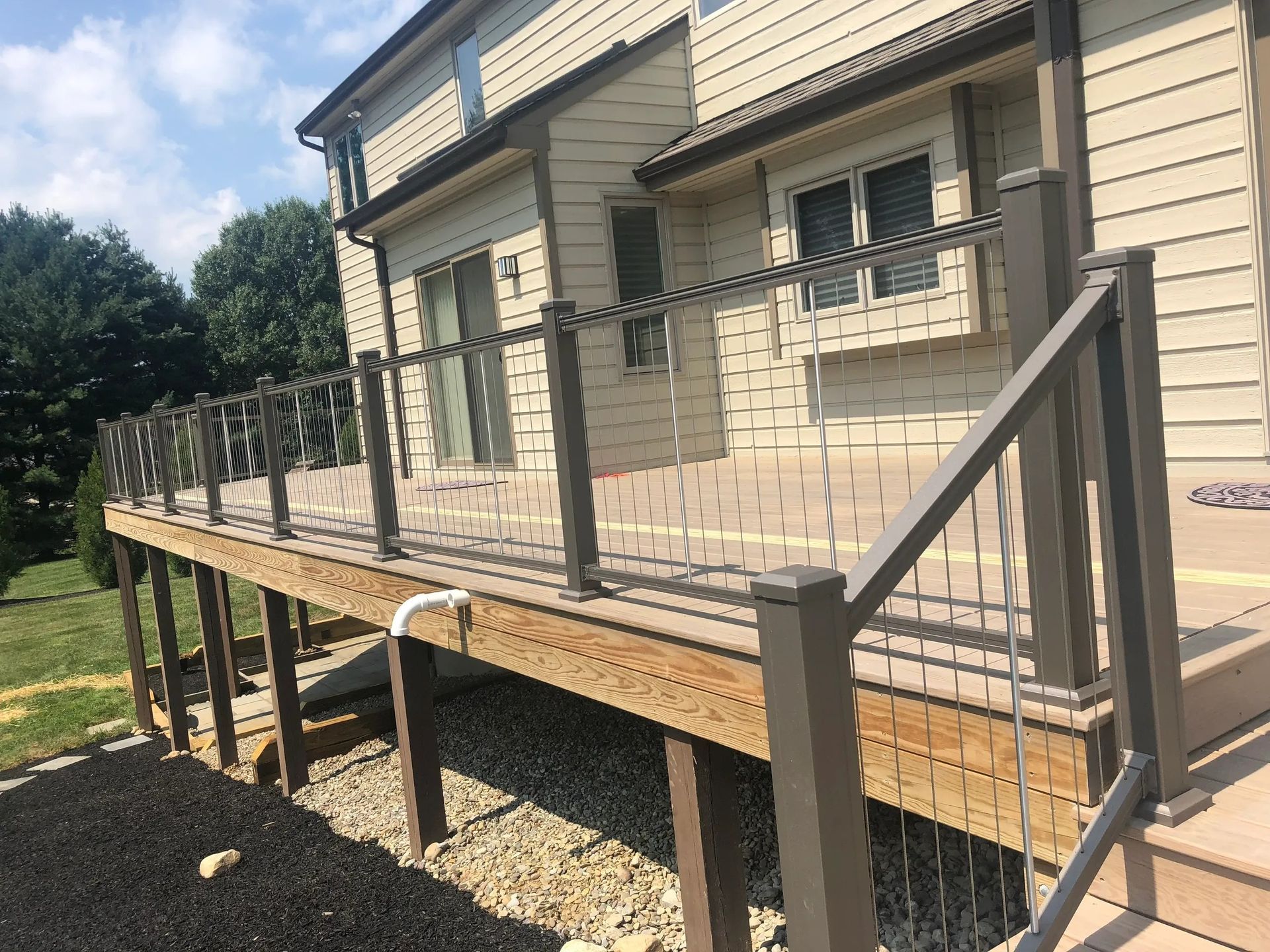 A wooden deck with a metal railing is in front of a house.