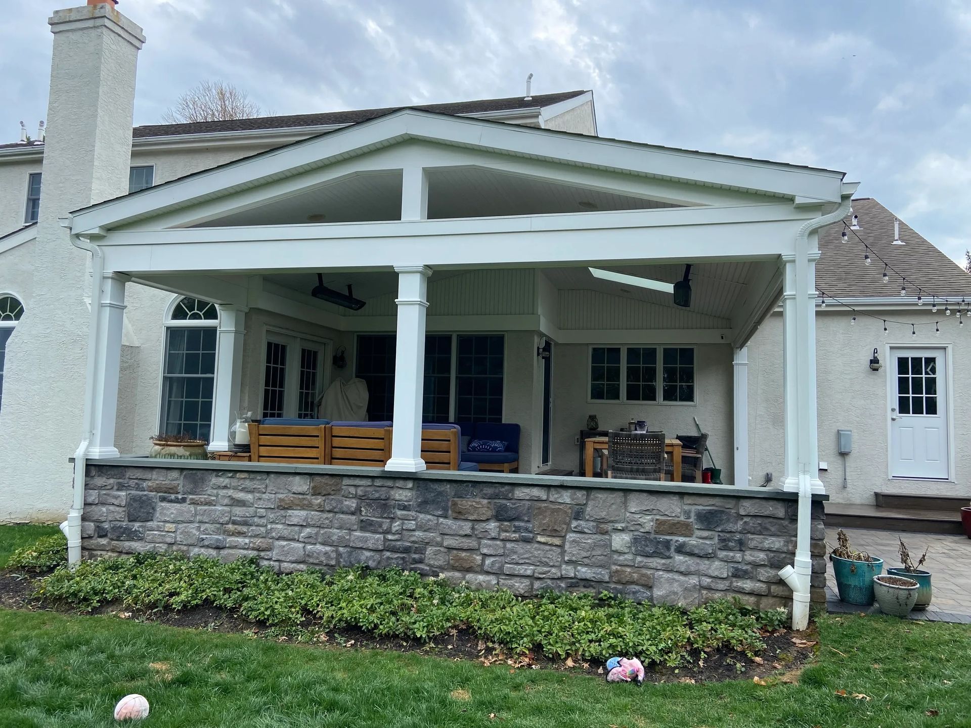 The back of a house with a porch and a stone wall.