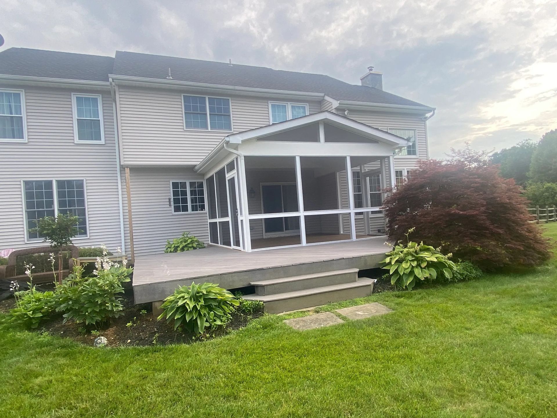 A house with a screened in porch and a large lawn in front of it.