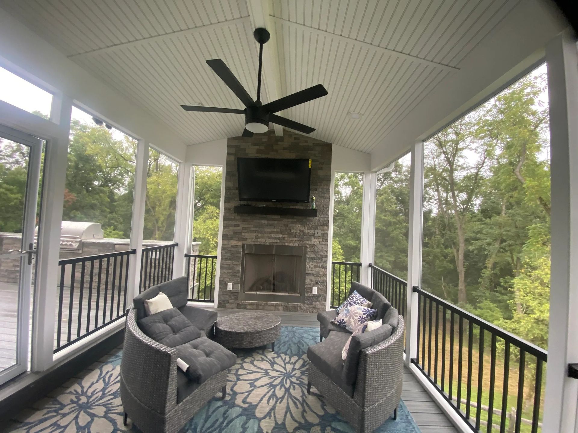 A screened in porch with a fireplace and a flat screen tv.