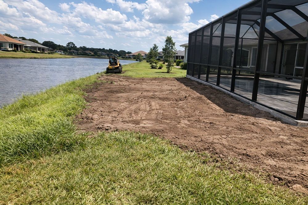 A construction site next to a lake. A small bulldozer is on the grass.