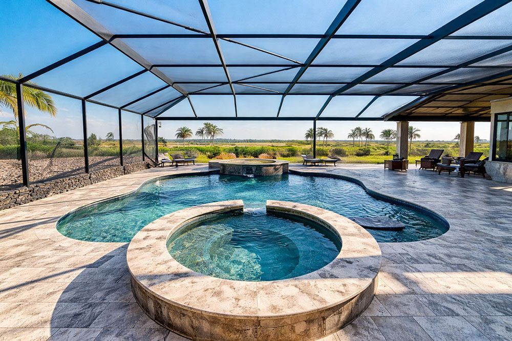 Swimming pool and spa surrounded by stone patio, under a screened enclosure.