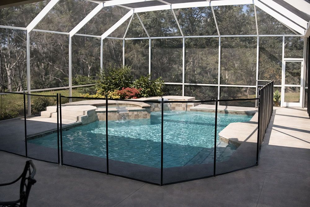 A pool enclosed by a black safety fence and a screened lanai with a lush outdoor view.