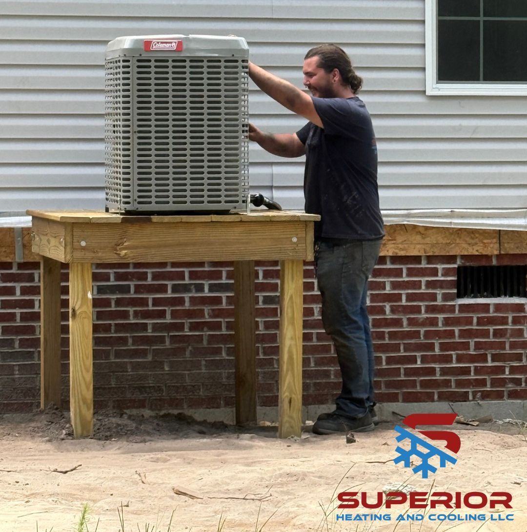 Four air conditioning units on a concrete pad, surrounded by gravel and greenery, against a tan building.