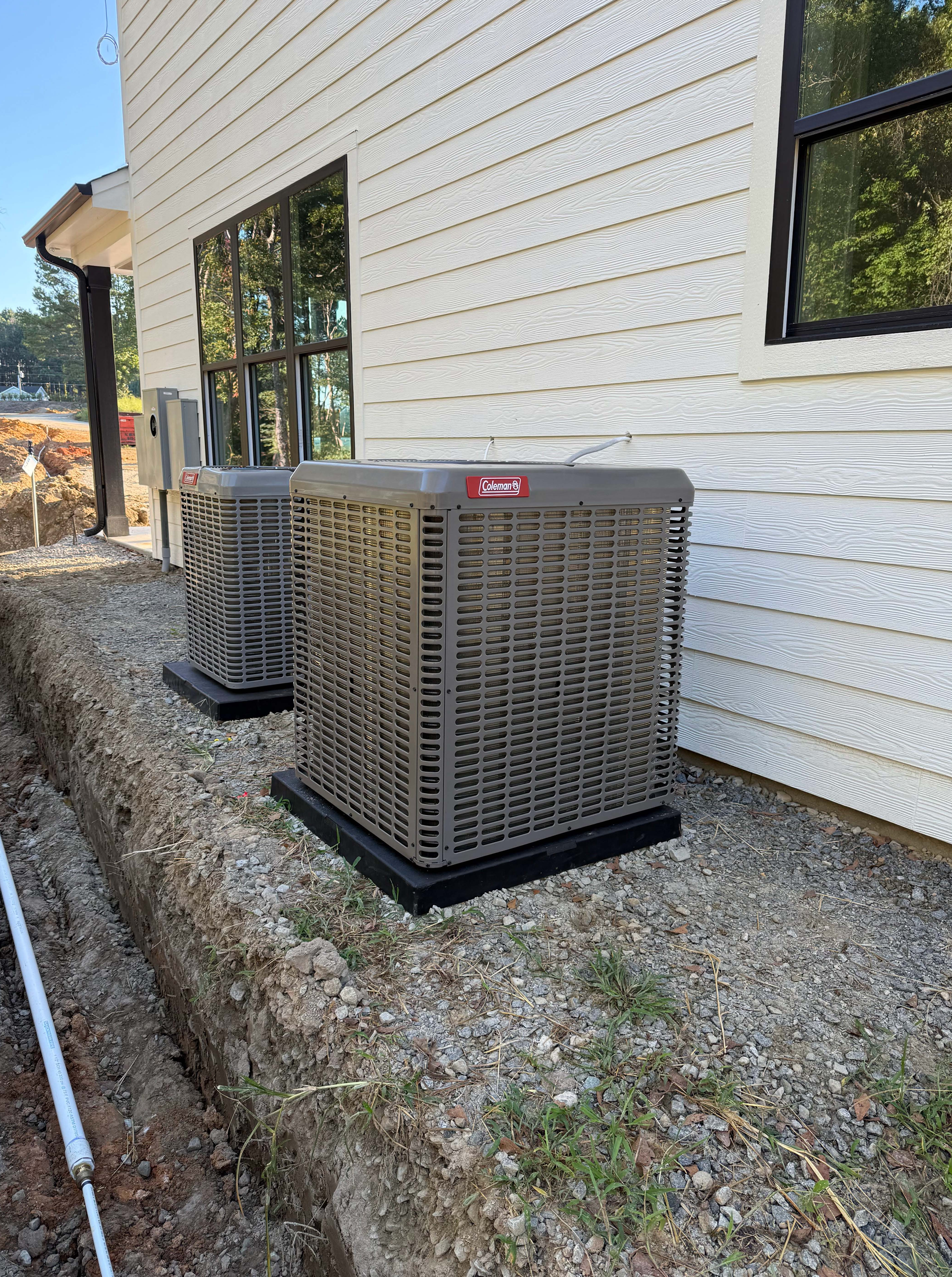 Two outdoor air conditioning units near a building with white siding.