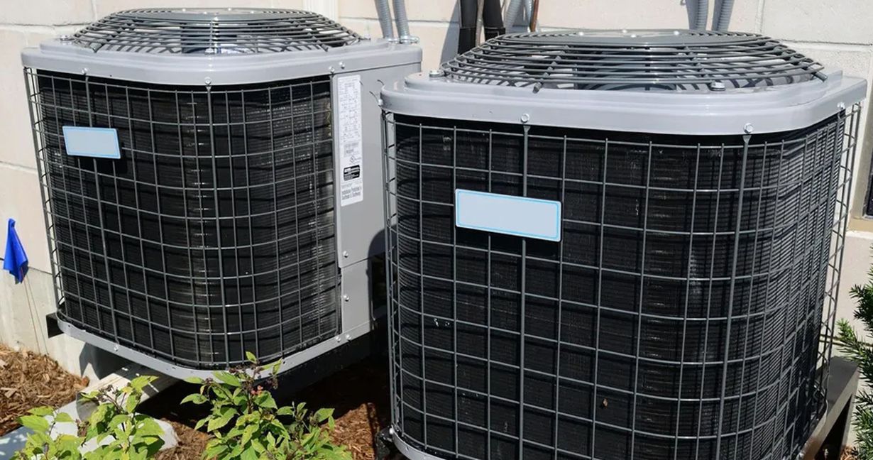 Blue furnace unit with open access panel in a basement, exposing internal components. The unit sits on a concrete base, with a metal tray below it.