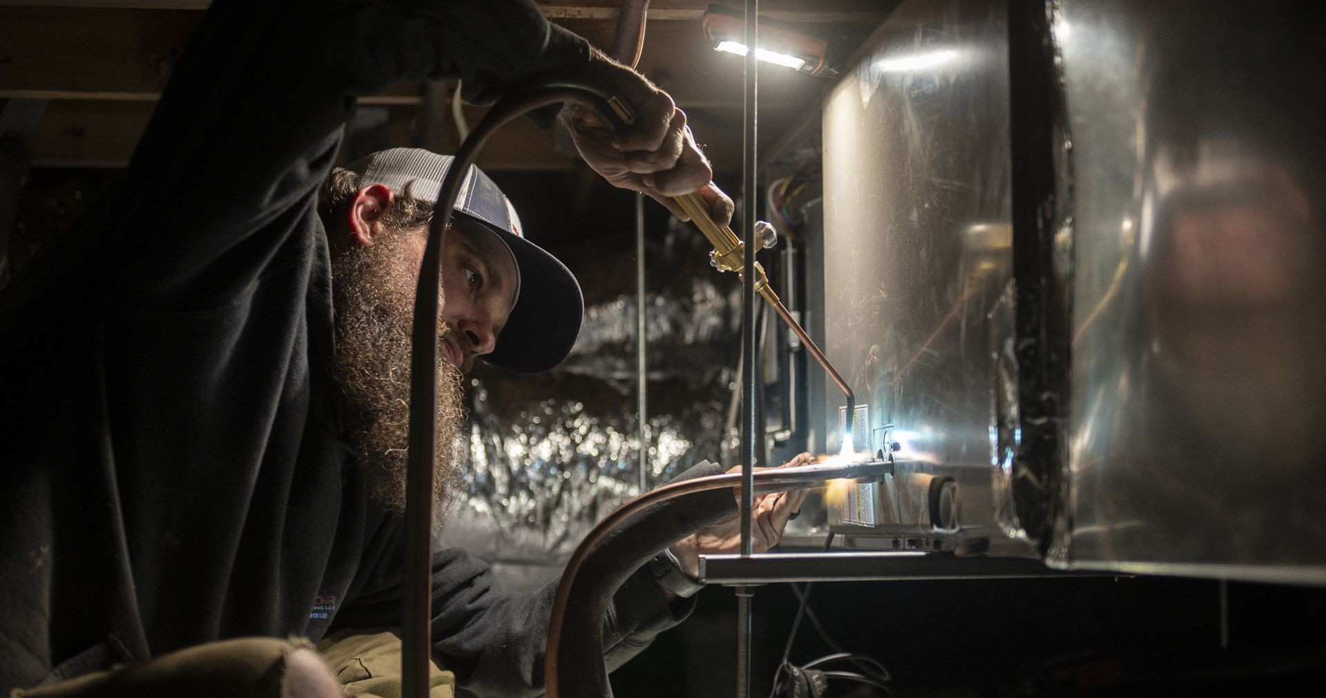 Hand holding a remote control aimed at a white air conditioner. The remote shows a temperature of 24 degrees.