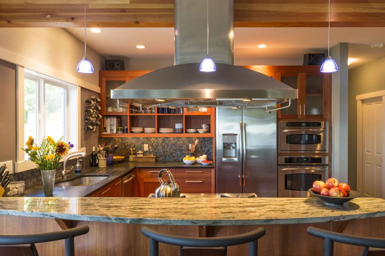 Modern kitchen with stainless steel appliances, wood cabinets, granite countertop, and hanging lights.