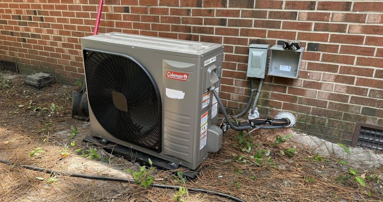 Two outdoor air conditioning units sitting on gravel next to a brown wooden fence.