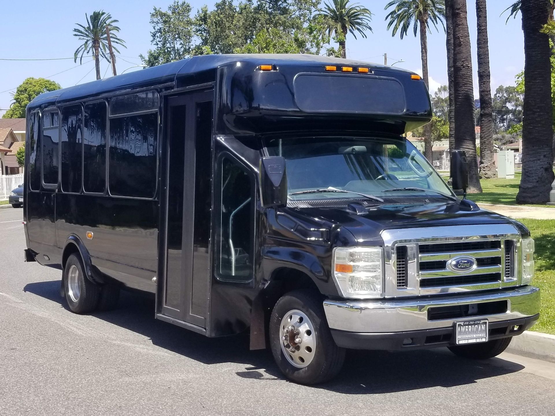 Black shuttle bus parked on a city street with trees in the background.
