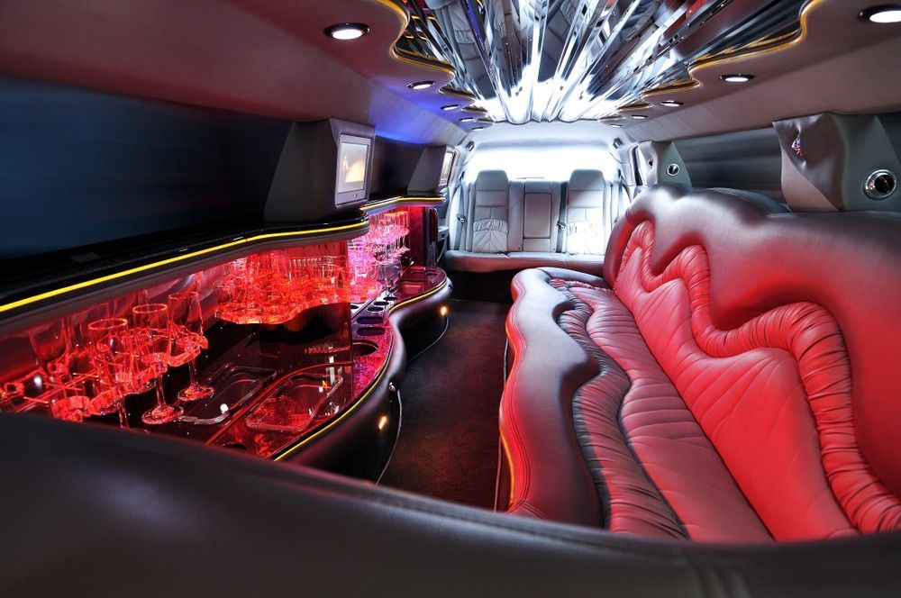 Interior of a limousine with red and blue ambient lighting, leather seating, and a bar area with glasses.