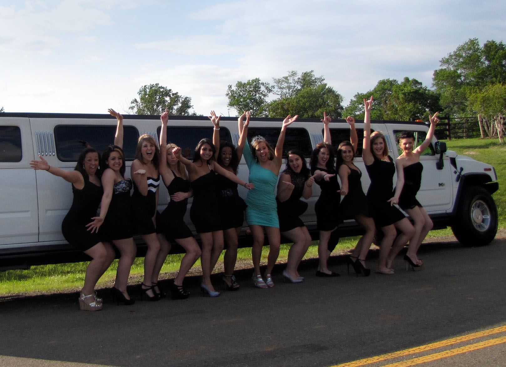 A group of women are posing in front of a white limousine.
