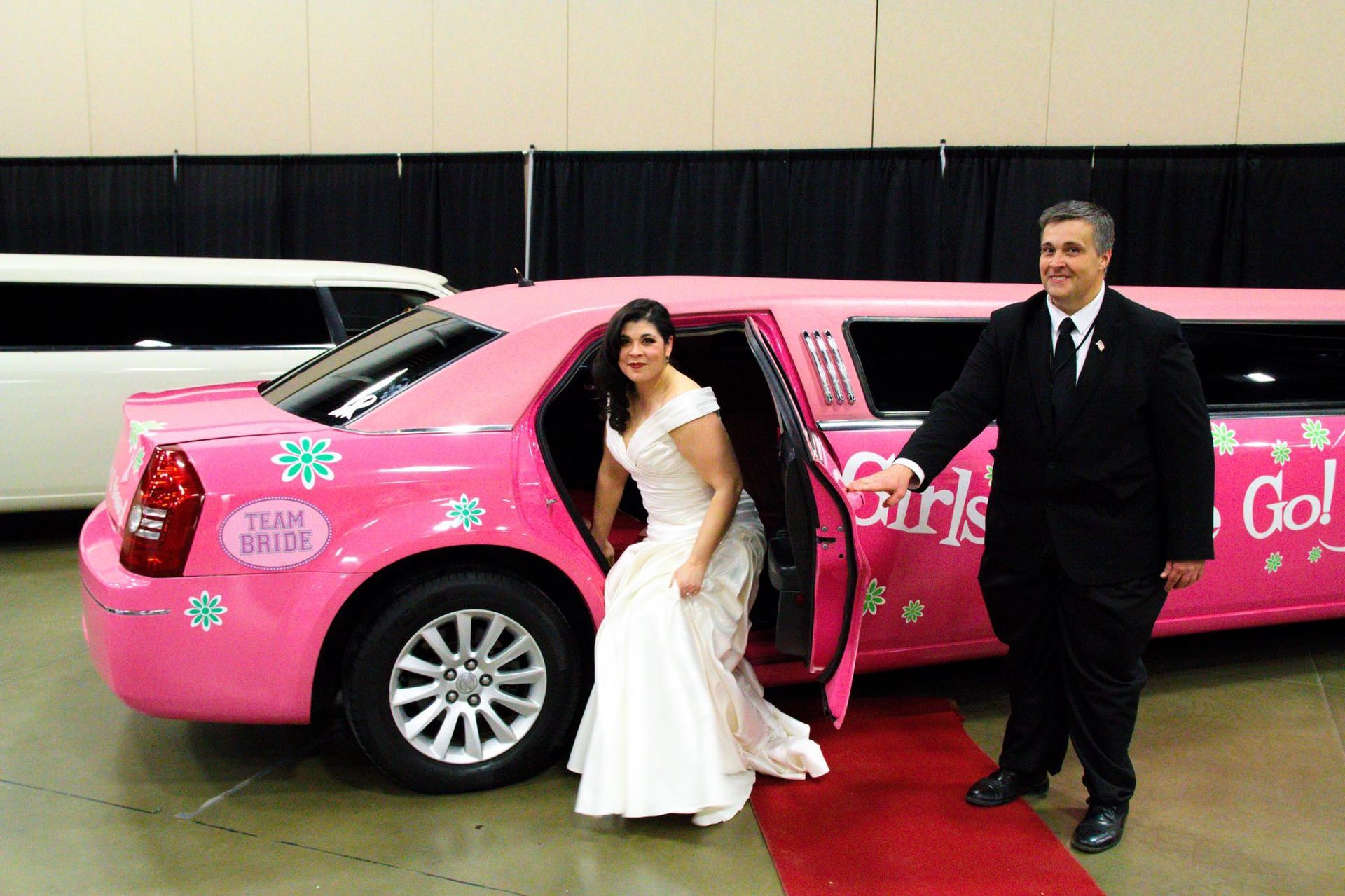 A bride and groom are getting out of a pink limousine.