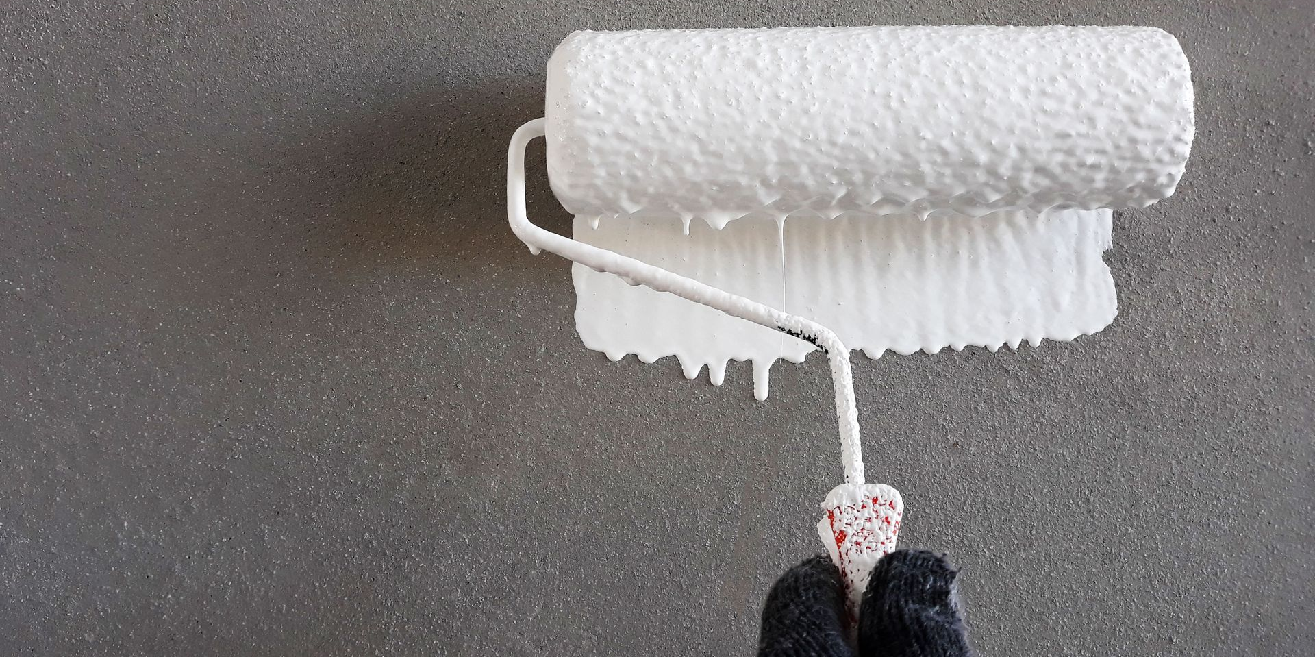 A person holds a white paint roller over a gray surface.