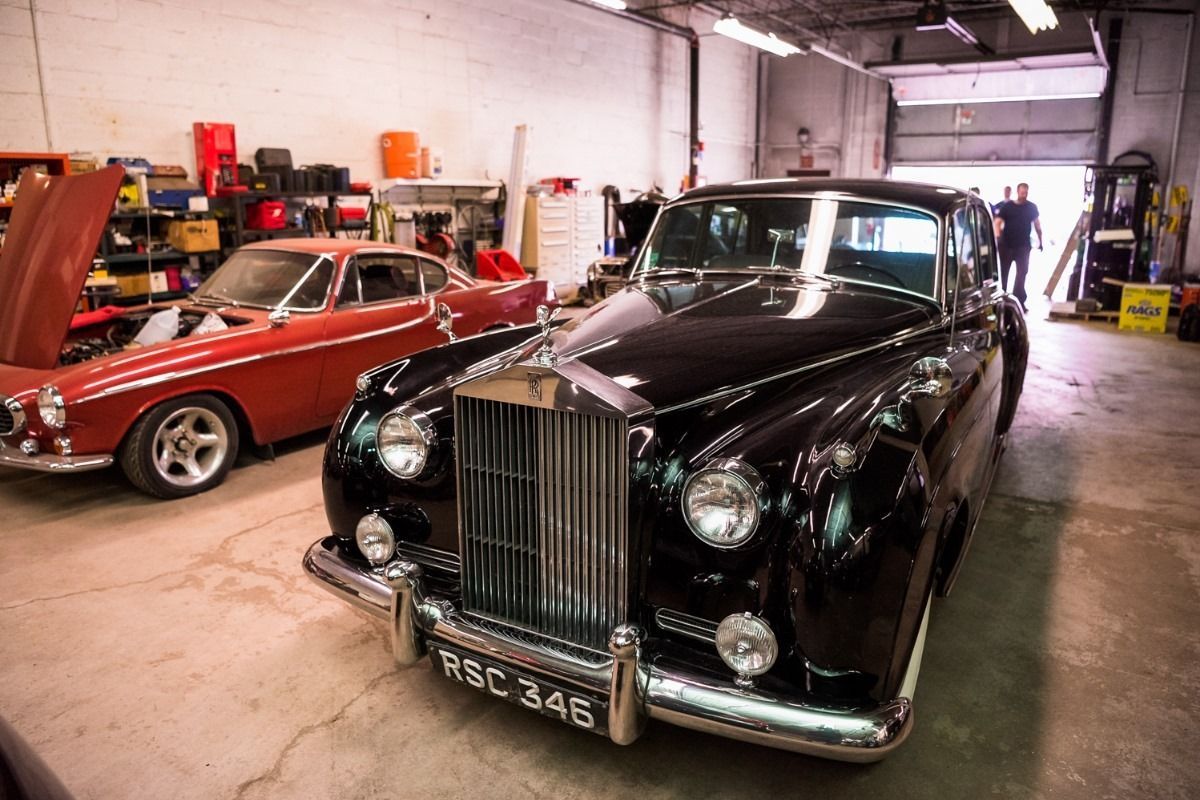 Classic black Rolls-Royce and red coupe parked in a garage workshop