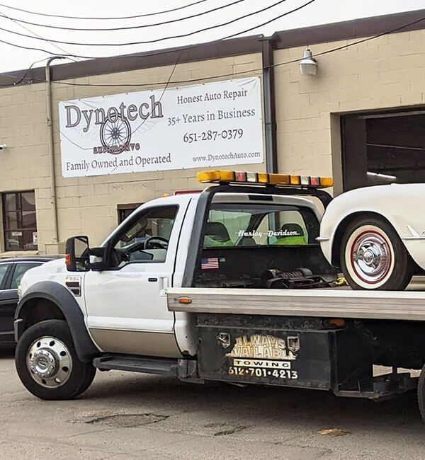 Dynatech towing truck parked outside an auto repair shop with a classic car on the flatbed.