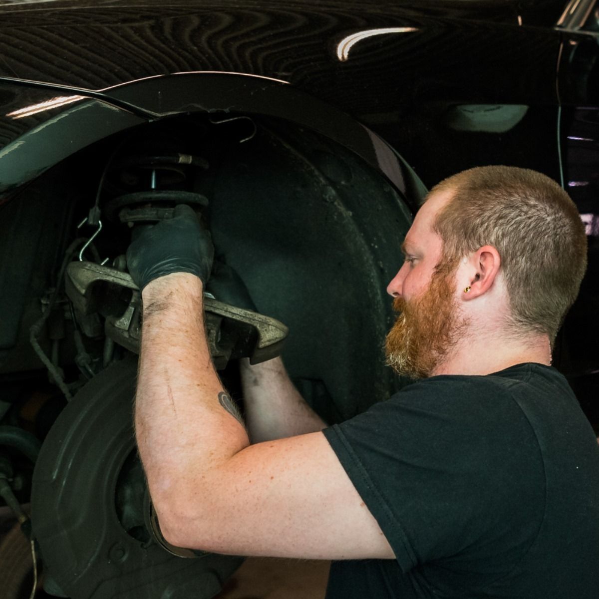 Mechanic working inside a car wheel well under a lifted vehicle