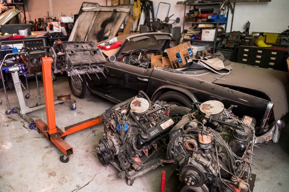 Workshop with a black car body, two engines in front, and tools scattered around a garage.