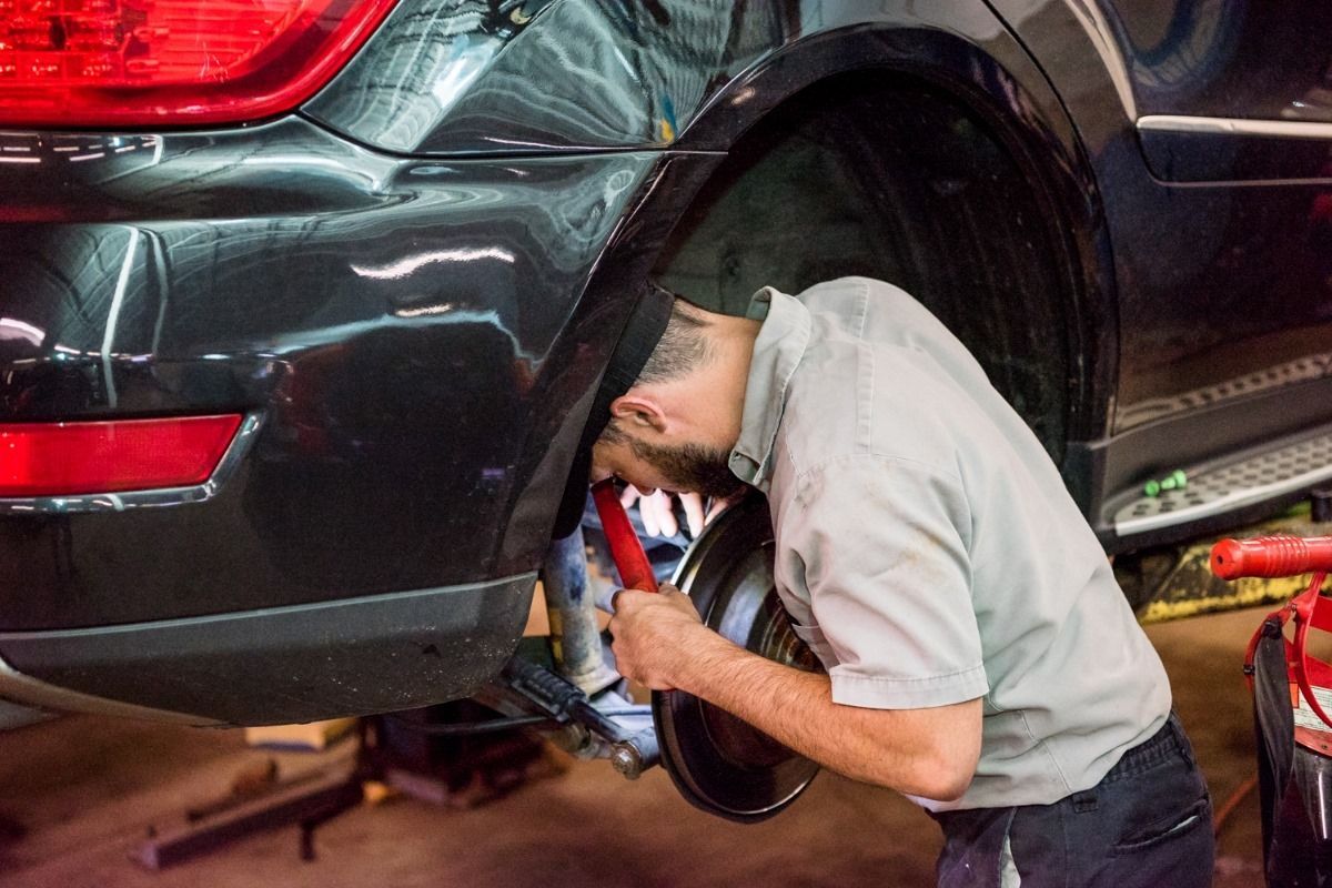 Mechanic working under the rear of a black SUV in an auto repair shop