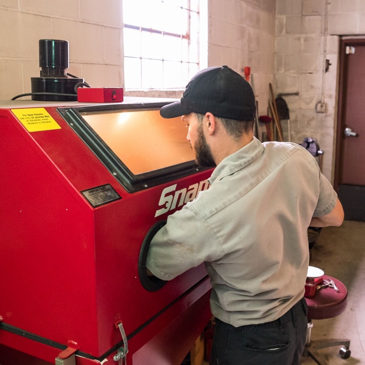Mechanic in gray coveralls works on a red Snap-on machine in a garage workshop.