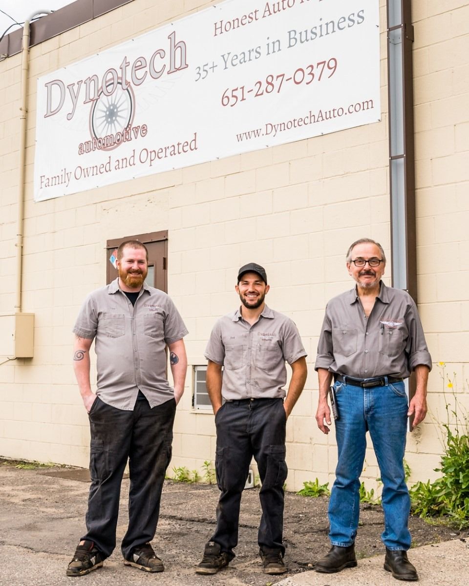 Three men stand outside a business building with a sign overhead.