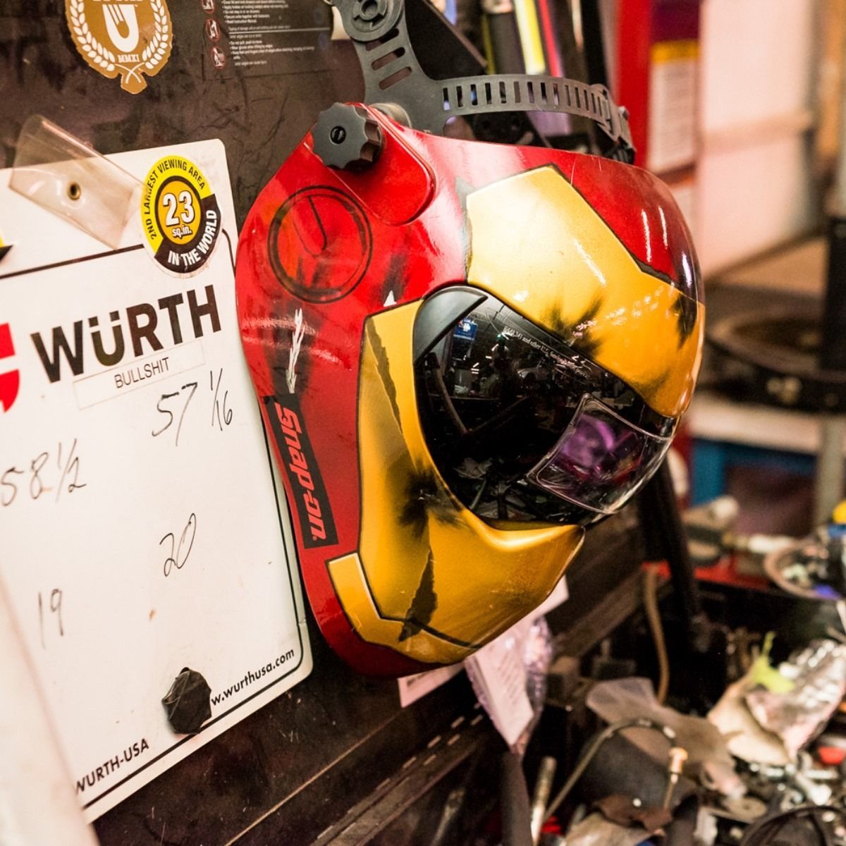 Red and yellow helmet-like object mounted in a cluttered workshop beside a Würth sign