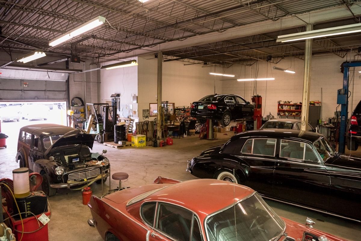 Auto repair shop with several classic cars, including a black sedan and a red car under repair.