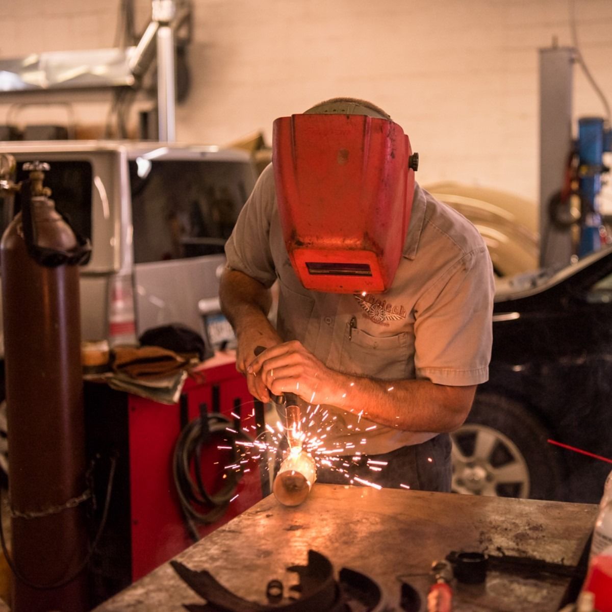 Worker in red welding helmet grinding metal in a workshop, sparks flying.
