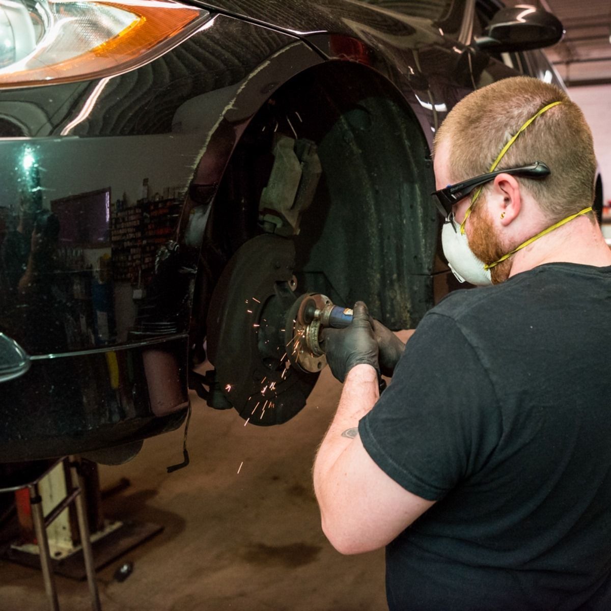 Mechanic wearing goggles and mask repairs a car wheel in a garage