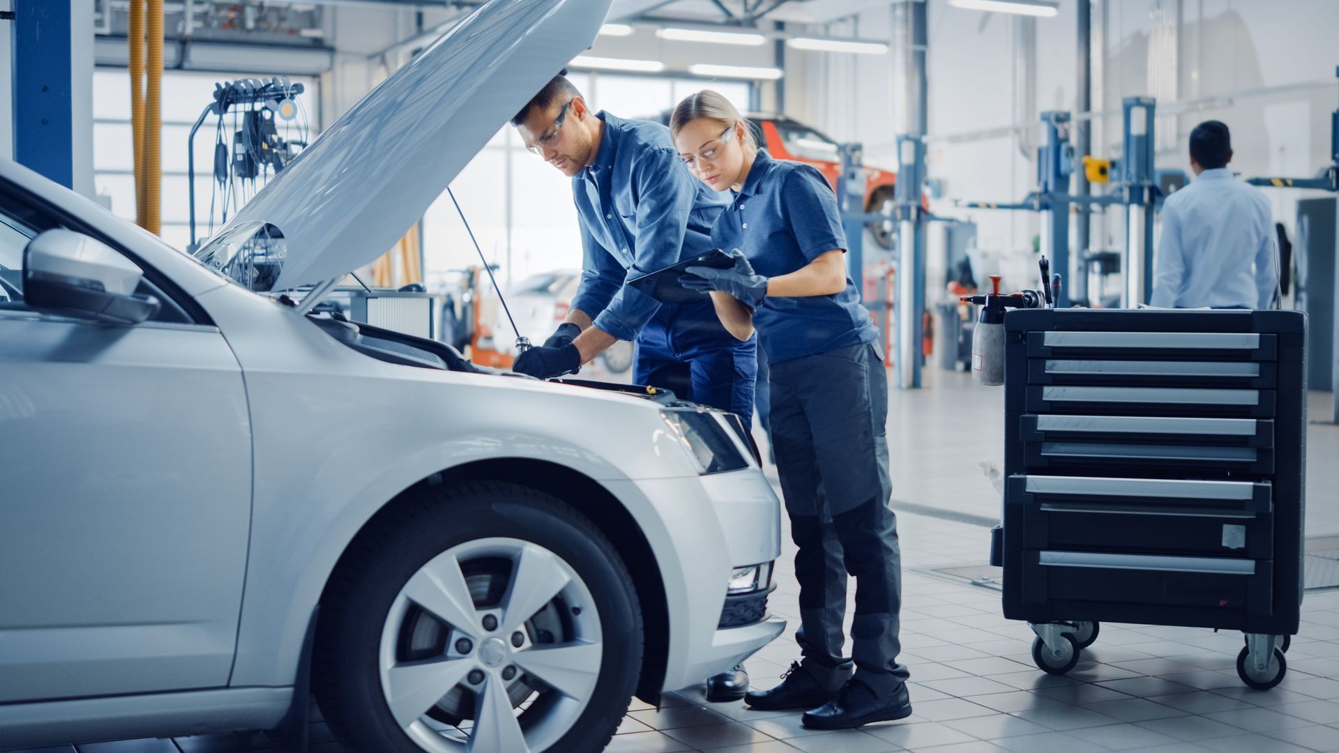 Mechanic inspecting a silver car with hood open in an auto repair shop