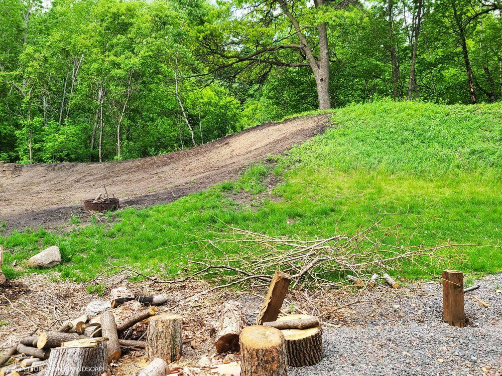A fire pit in the middle of a grassy field with trees in the background.