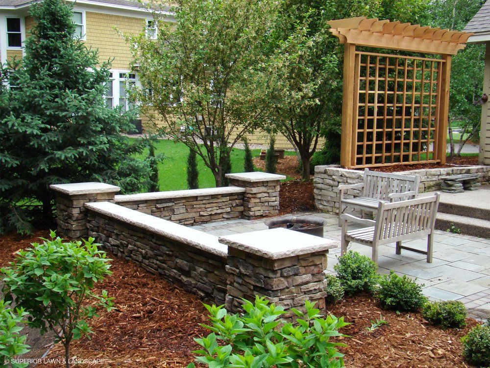 A stone wall surrounds a fire pit in a backyard.